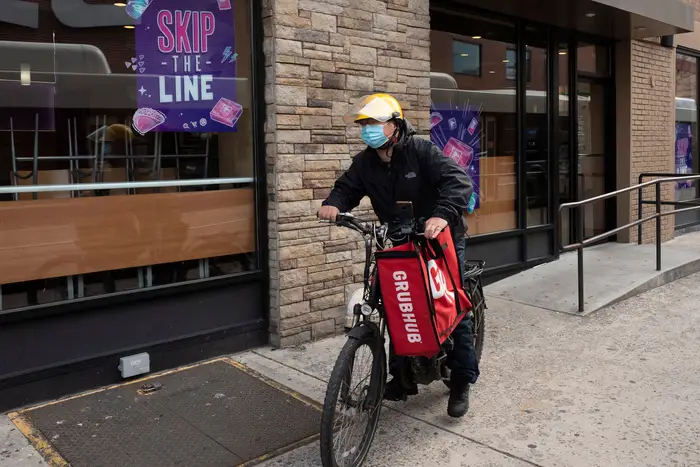 A food delivery worker with a GRubhub branded bag and a bicycle on a sidewalk